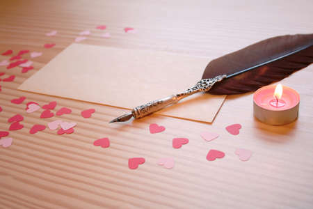 St Valentine's day: a love note for the loved one, with a quill, pink and red hearts and a candle on a wooden tableの写真素材