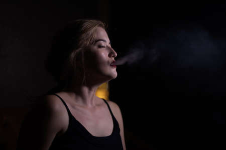 Beautiful girl with red lips blows smoke from a hookah from her mouth in cafeの写真素材