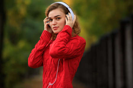 Happy woman in red pullover listening music through headphones in the autumn parkの写真素材