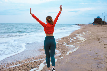 Woman in orange t-shirt with raised hands up enjoying the sea