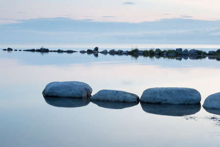 Breakwater Rocks in Calm Sea with clouds and reflextions in the water.の写真素材