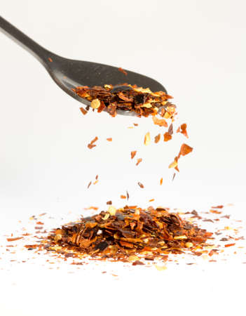 Dried Chili Pepper Falling from Tablespoon into pile of chili pepper on a white background.の写真素材
