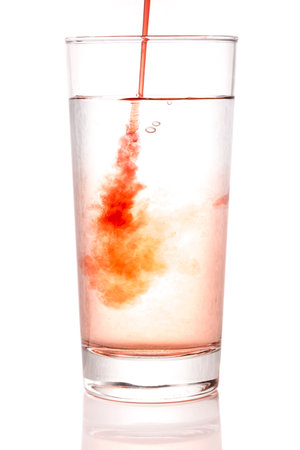 Pouring Squash into Glass of Water close up with a white background.の写真素材