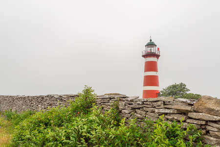 Red and White Striped Lighthouse with grass and a cloudy sky.の写真素材