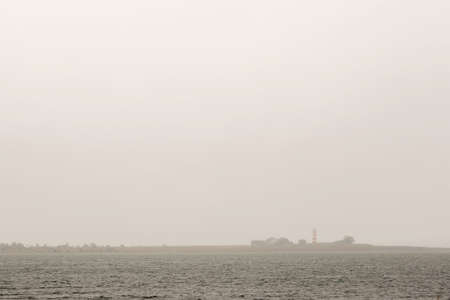 Red and White Striped Lighthouse by ocean and a cloudy sky.の写真素材
