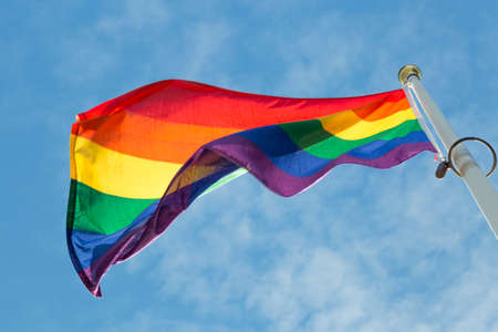 Rainbow Flag waving in the wind with a partly cloudy sky.の写真素材