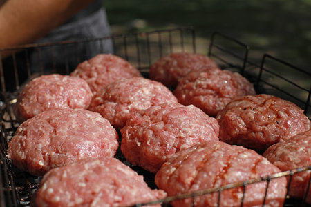Raw minced meat for homemade grilled hamburgers. Several fresh and juicy hamburgers cooking on a fire grillの写真素材