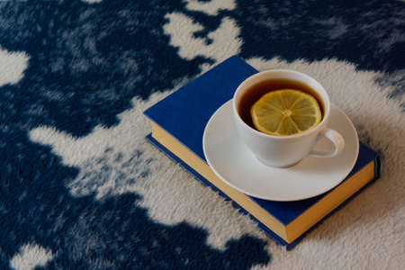 White cup of tea with lemon and blue book on the white-blue blanketの写真素材