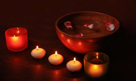 Glass candlesticks and candles and wooden bowl of water with petals on wooden tableの写真素材