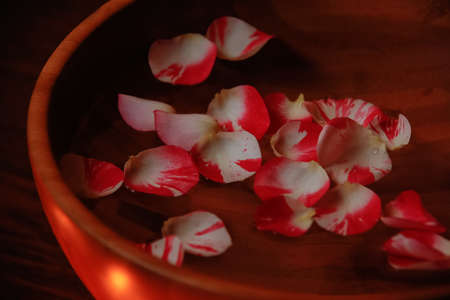 Rose petals in bowl with water on wooden tableの写真素材