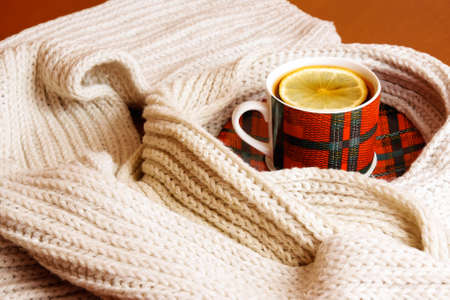 Red-green cup of tea with lemon and gray scarf on wooden tableの写真素材