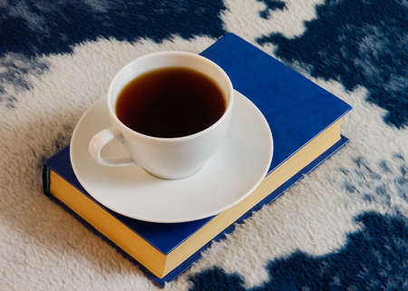 White cup of tea and blue book on the white-blue blanketの写真素材