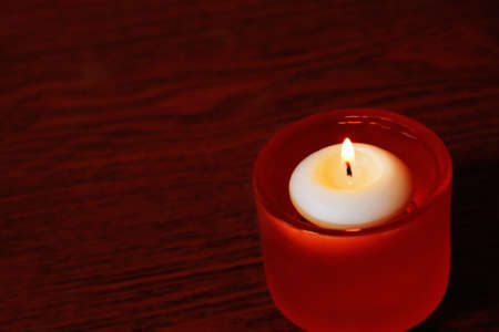 Single candle  in orange glass candlestick on a dark wooden table. Close up shot with selective focus.の写真素材
