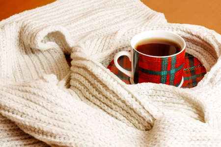 Red-green cup of tea and gray scarf on wooden tableの写真素材