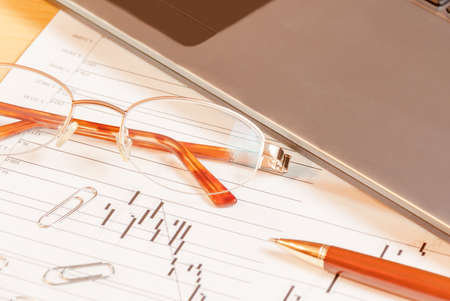 Laptop, pen and glasses on office desk. Selective focus on glassesの写真素材