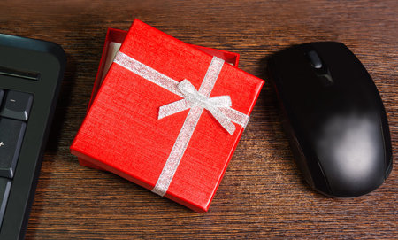 Composition with red gift box,  mouse and keyboard laying on wooden deskの写真素材