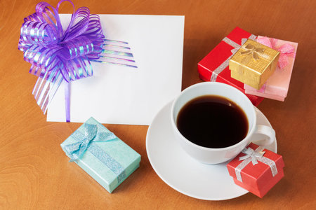 Blank greeting card with bow,  colored gift boxes  and white coffee cup on wooden backgroundの写真素材
