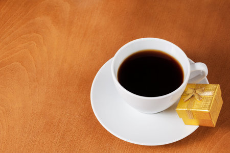 White coffee cup and gold gift box with bow on wooden backgroundの写真素材