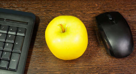 Composition with green apple,  mouse and keyboard laying on wooden desk. Selective focus on appleの写真素材