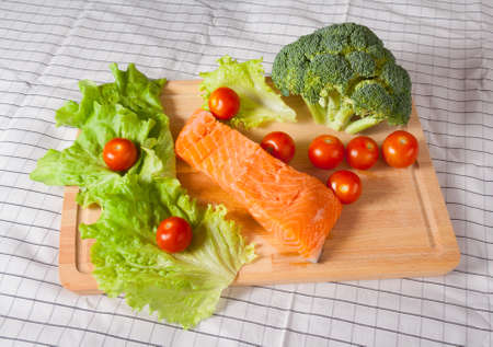 Fresh salmon with tomatoes, broccoli and salad on a cutting boardの写真素材