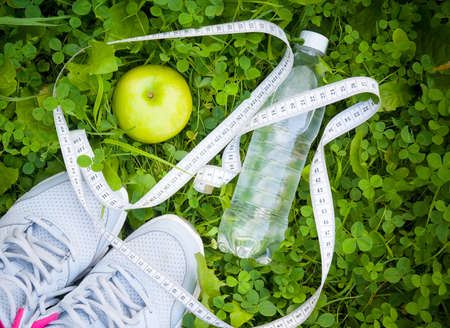 Sports shoes sneakers, bottle of water and apple on fresh green grass. Sports in the open air. top viewの写真素材