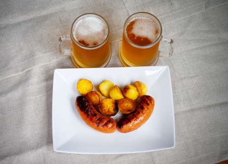 Pork sausages on a white plate , mugs of beer, roasted potatoes. Top viewの写真素材