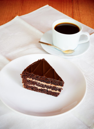 Chocolate cake on the white plate with cup of coffee. Selective focus on cake