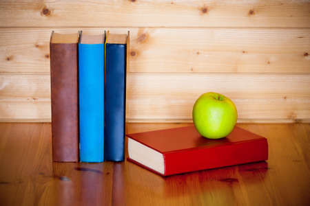 Books and green apple on wooden table over wooden backgroundの写真素材