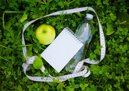 Bottle of water, measuring tape and apple on  green grass