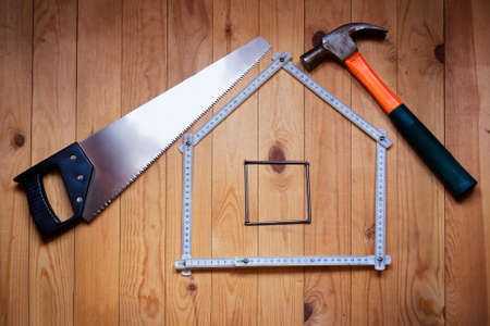 Set of different work tools are in  form of  house: hammer, hand saw, meter, nails over  wooden background. House concept. Build a house. Repairs.の写真素材