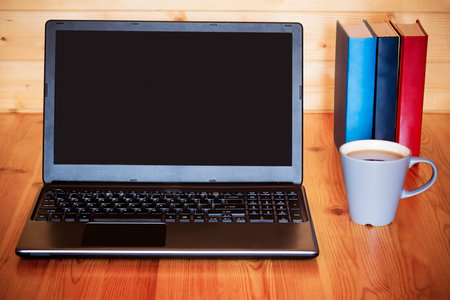 Laptop, cup and books on wooden table