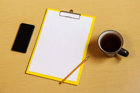 Clipboard with white sheet, cup of tea, smartphone and pencil on deskの写真素材