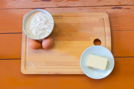 Eggs, butter, flour and cutting board on painted wooden background