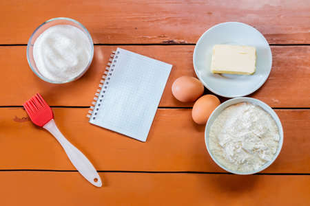 Eggs, butter, flour, sugar and notebook on painted rustic wooden background.の写真素材