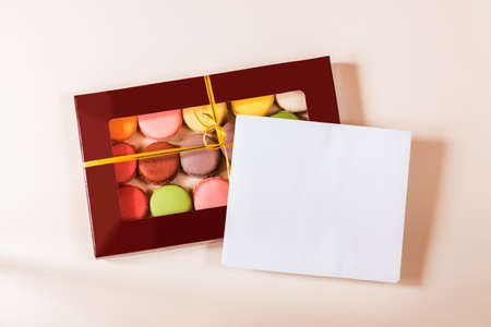 Note card and different colorful macaroons in gift box on beige backgroundの写真素材