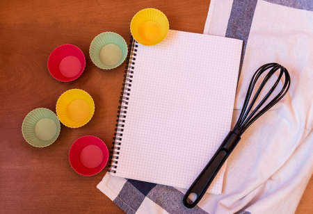 Whisk, cupcake silicon baking cups and empty notebook on wooden backgroundの写真素材