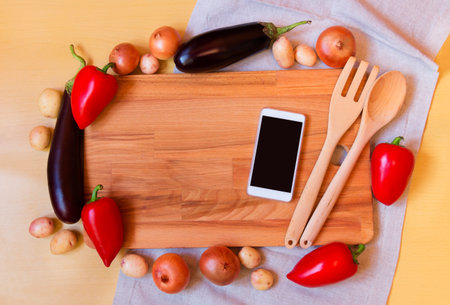 High angle still life view of wooden spoon, fork  and wooden cutting board surrounded by assortment...