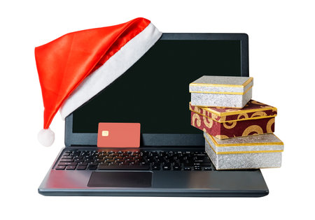 Opened laptop with red santa claus hat put on monitor corner, credit card  and gift boxes isolated...