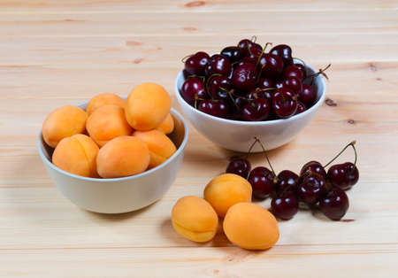 Two bowls full of fresh apricots and cherries berries on wooden background. の写真素材