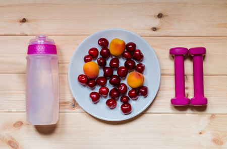 Dumbbells, bottle of water, fresh fruits on wood background. Top view