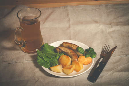 Mug of beer with plate of grilled sausages and roasted potato on tableの写真素材