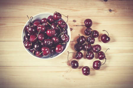 Fresh ripe cherries berries in white bowl on wooden background. Top view.の写真素材