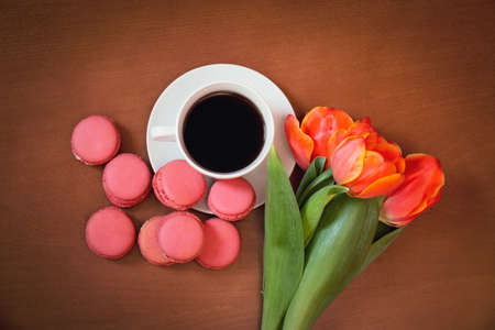 Cup of coffee with pink macaroons and tulip flowers on wooden background. Top view.の写真素材