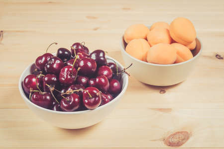 Bowls full of fresh cherries berries and apricots on wooden background. Selective focus.の写真素材
