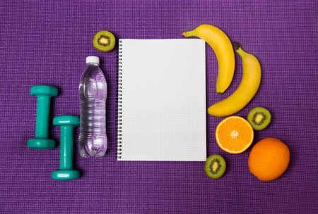 Bottle of  water, fruits, notebook and  dumbbells on yoga mat background