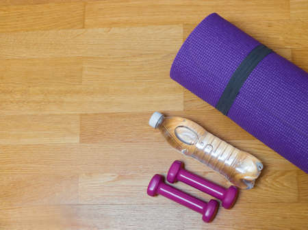 Yoga mat, dumbbells and bottle of water on wooden floor. Top view with copy space.の写真素材