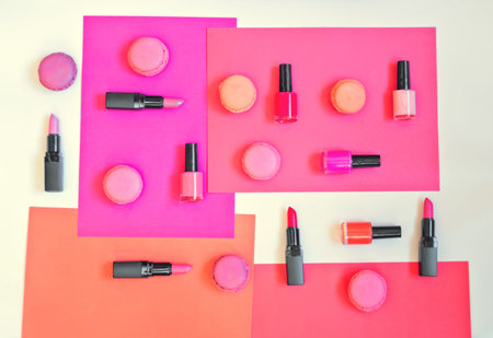 Collection of various lipsticks, nail polishes and macaroons on colorful paper background
