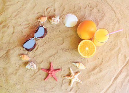 Glass of orange juice, oranges, sunglasses, starfishes and seashells on sand beachの写真素材