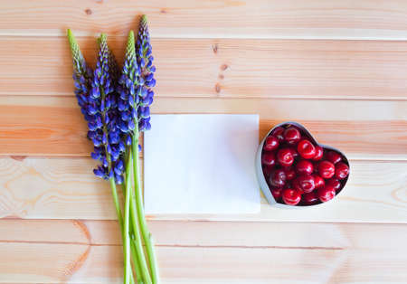 Blue wildflowers lupine, heart shape gift box with fresh cherry and empty card for your text on wooden background.の写真素材