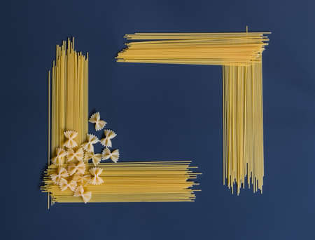 Raw pasta spaghetti and farfalle in shape of frame on dark background.の写真素材